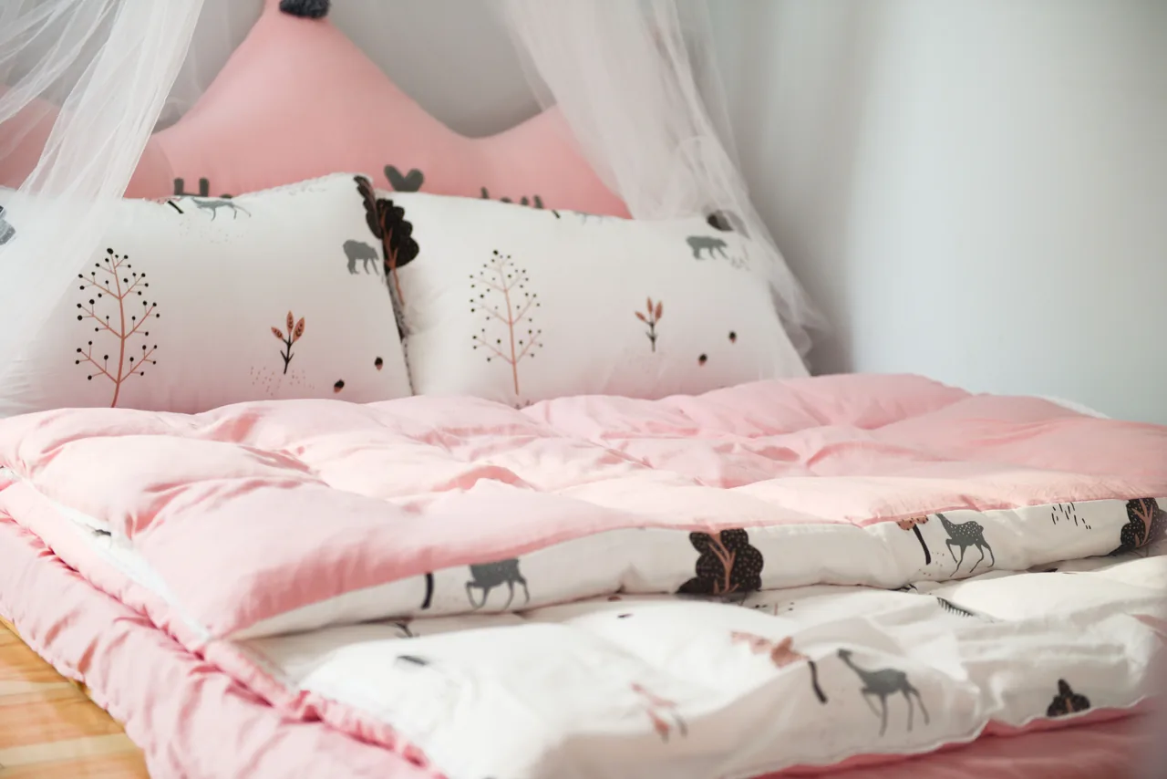 Pink and white baby bedding set with a quilted duvet and pillows printed with trees and deer