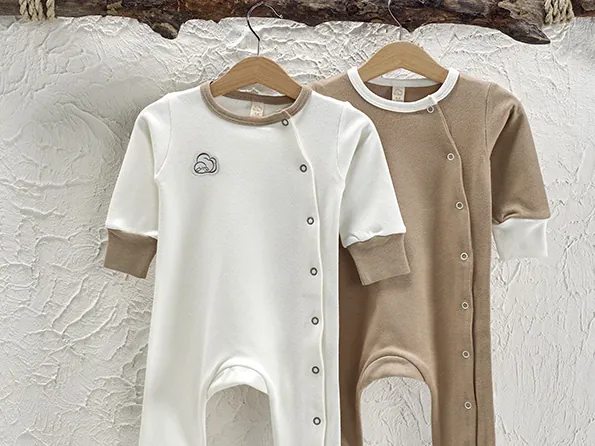 Two baby jumpsuits in cream and light brown hanging on wooden hangers