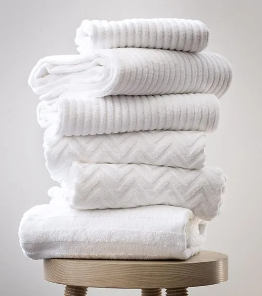 Stack of white towels with a wave-textured weave on a wooden stool
