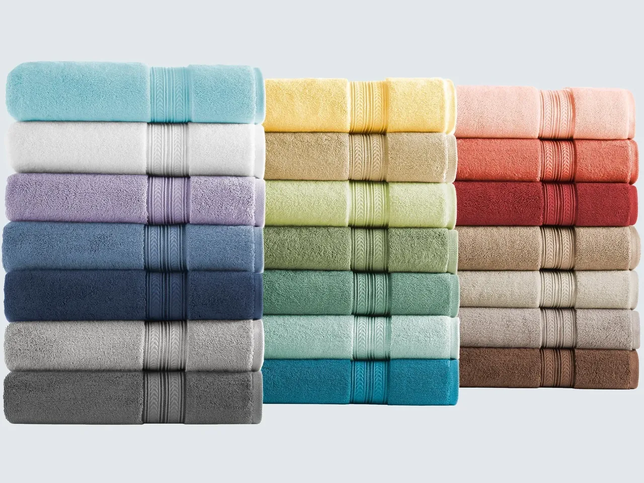 Stacks of cotton bath towels with woven borders in many colours, from white and grey to coral and teal