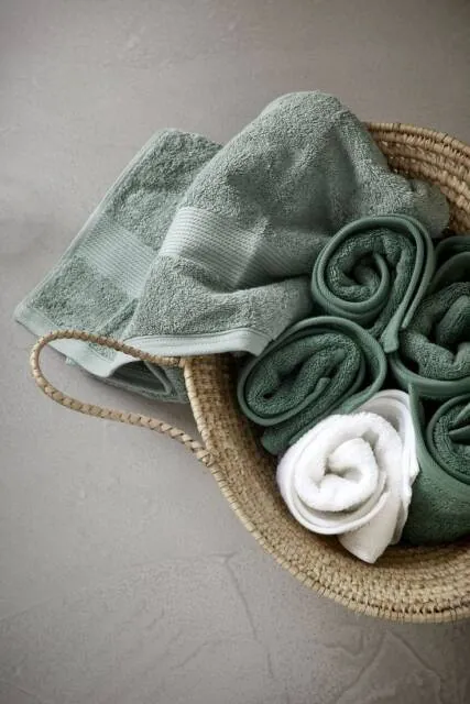 Rolled green and white hand towels in a woven basket