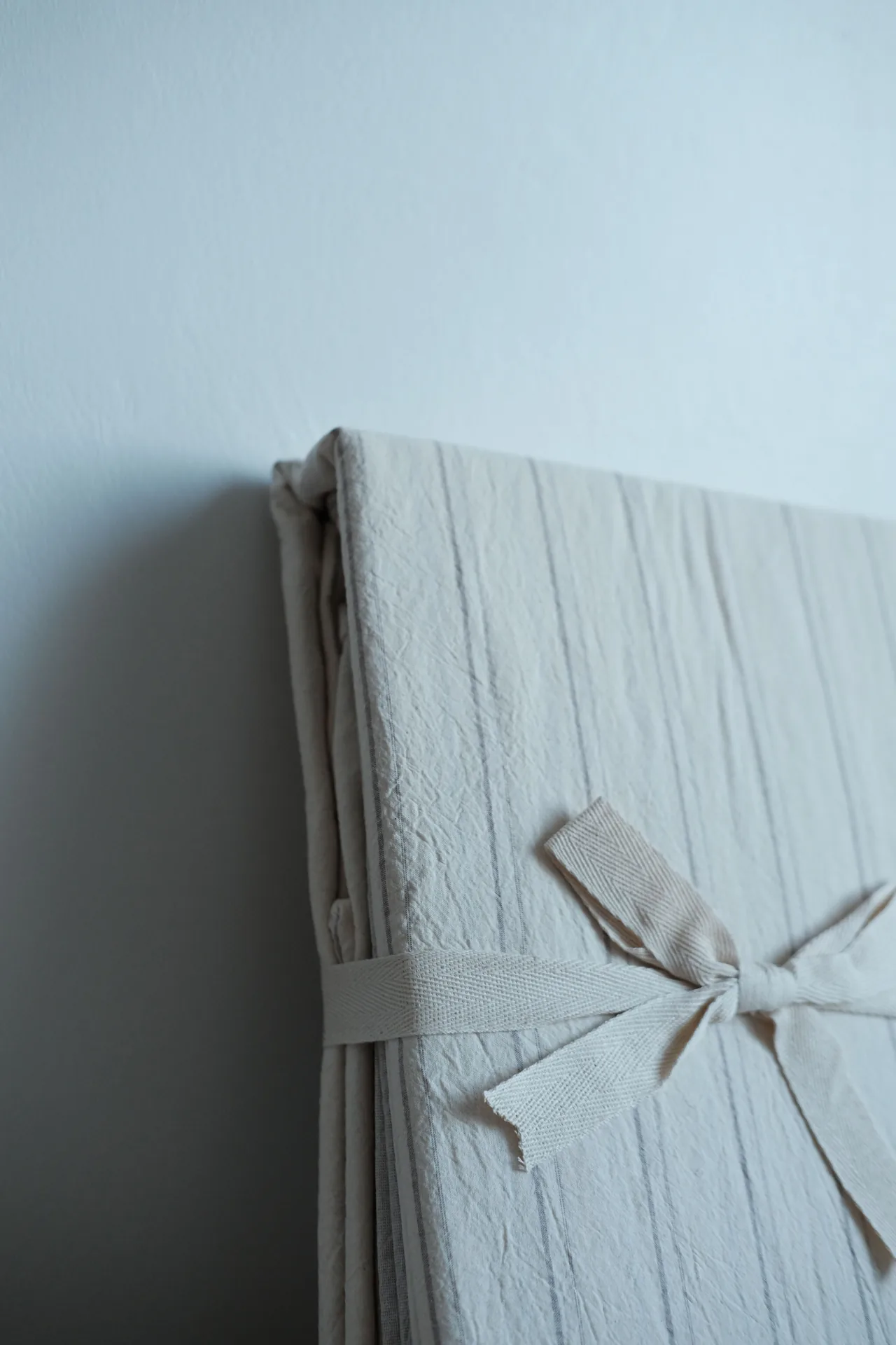 Folded cream duvet cover set with thin grey stripes, tied with a fabric ribbon