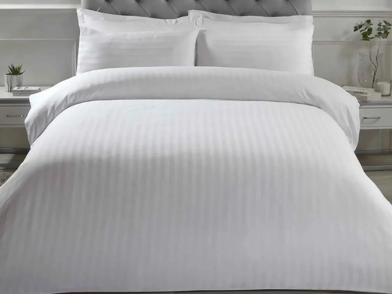 Hotel room with a made double bed in white linen, pillows and a dark bed runner