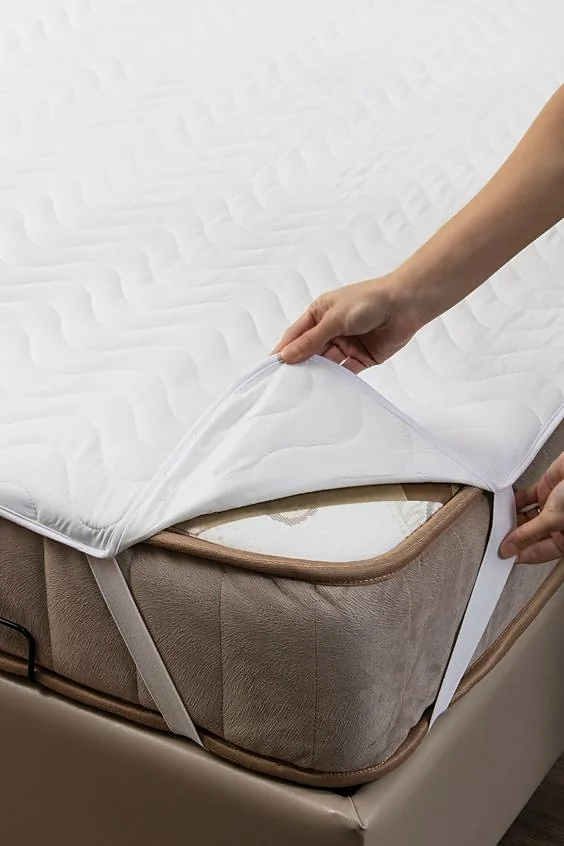 Hand lifting the corner of a quilted mattress protector held by an elastic corner strap