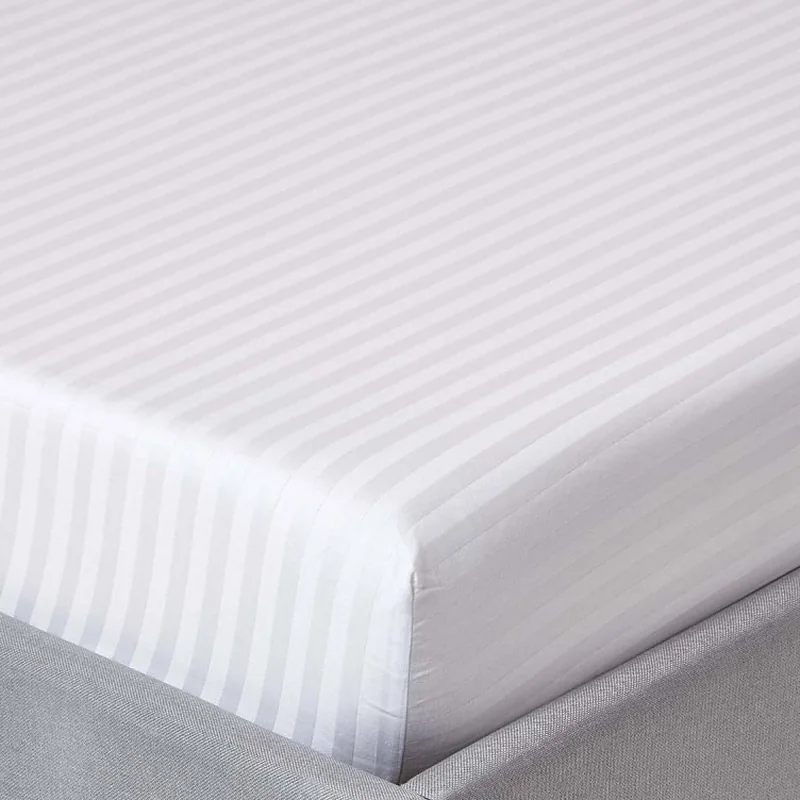 Corner of a white stripe satin fitted sheet on a mattress