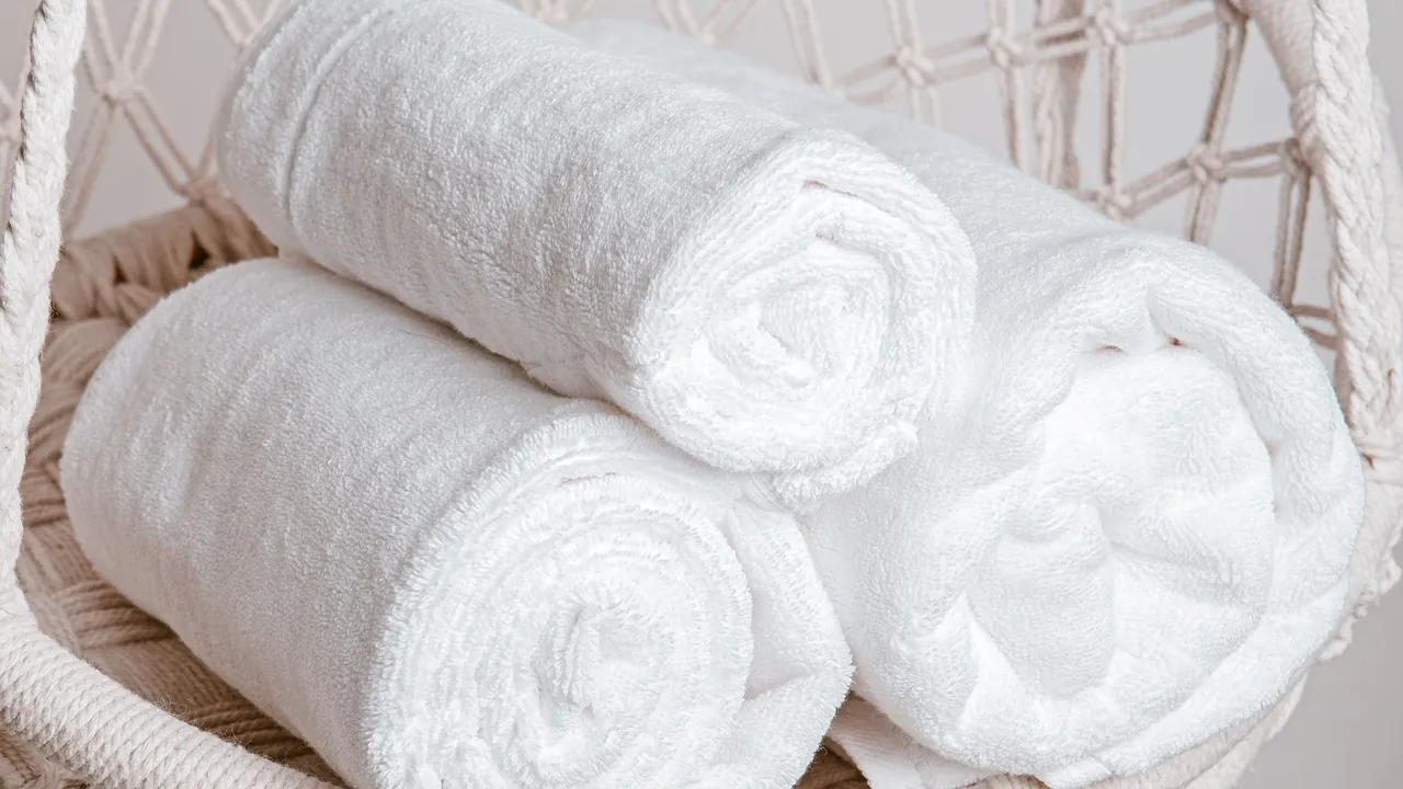 Three rolled white terry towels in a woven basket
